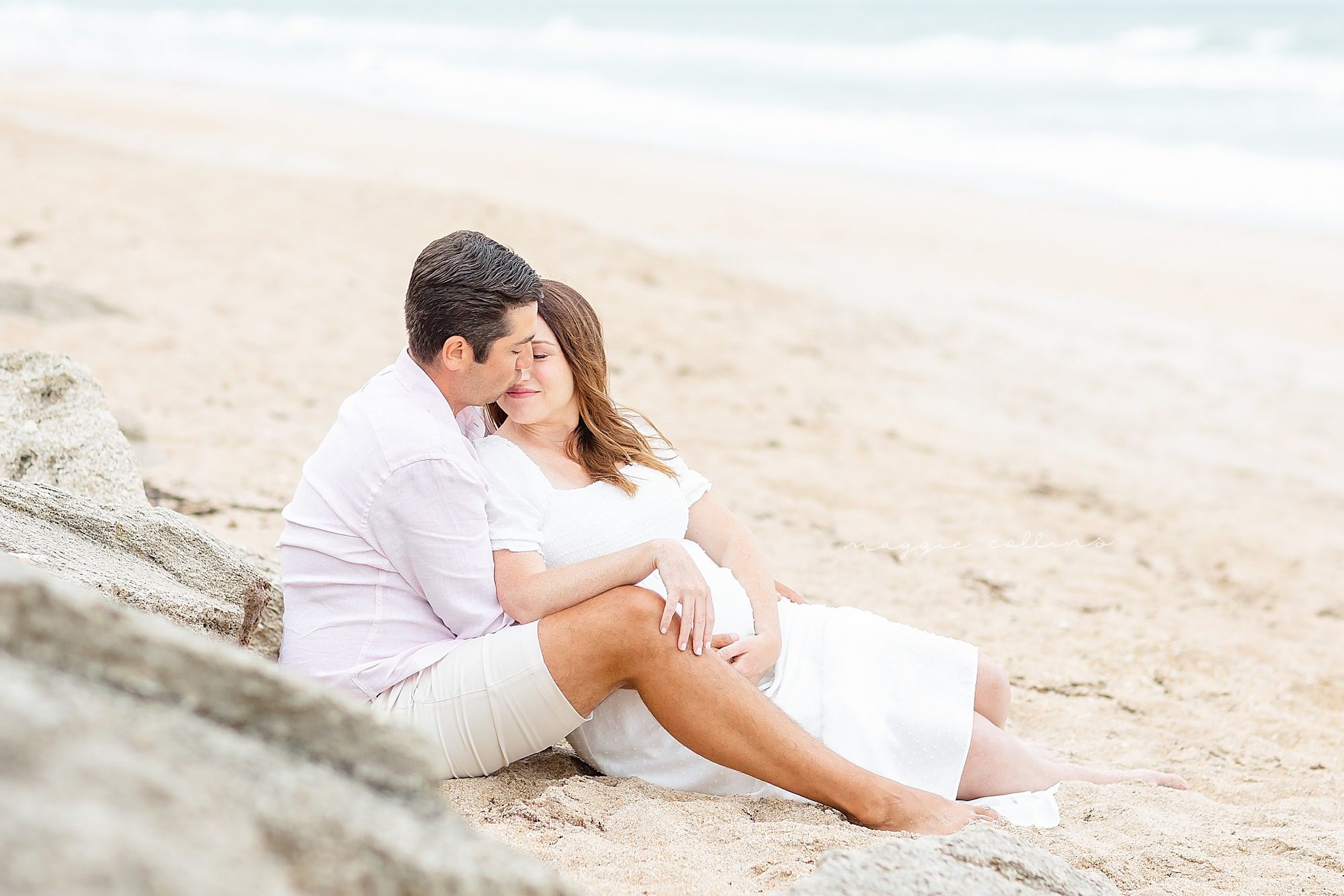 Maternity couples snuggled up on the beach sand.